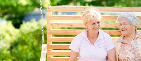 Pflegerin und Seniorin lachend auf einer Bank im Mühlhofer Stift Bayreuth