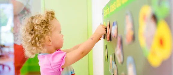 Mädchen in der Kinderkrippe hängt Bild an Magnetwand auf