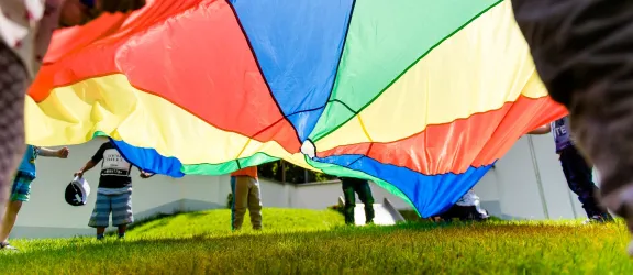 Kindergartenkinder spielen mit buntem Schwungtuch im Garten