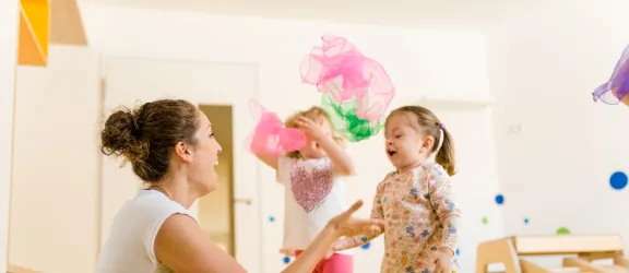 Erzieherin spielt mit Mädchen und Tüchern in der Kinderkrippe