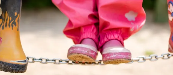 Kinder in Gummistiefel auf Balancierkette im Kindergarten