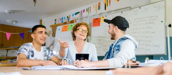 Zwei junge Geflüchtete mit Lehrerin beim Deutschkurs in der Clearingstelle