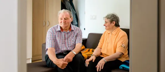 Zwei Menschen mit Behinderung sitzen auf dem Sofa in einer Wohngruppe