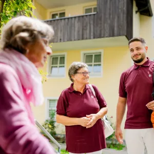 2 ambulante Pflegefachkräfte mit Seniorin vor dem Haus