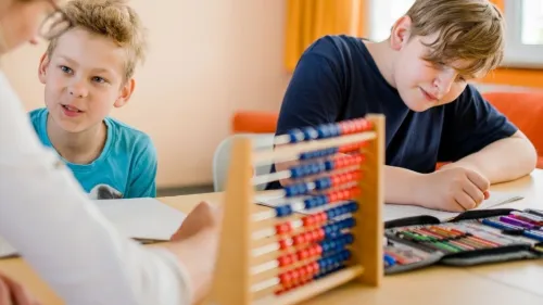 Zwei Schüler und eine Lehrerin bei den Hausaufgaben mit einem Abakus