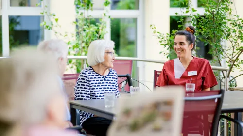 Pflegefachkraft und Bewohnerinnen im Gespräch im Garten