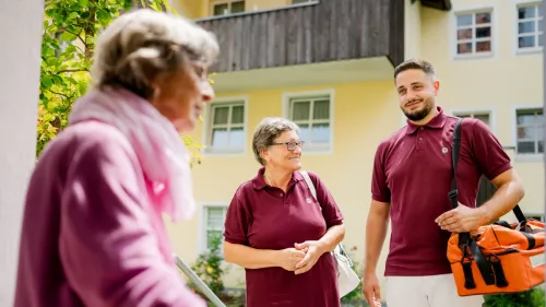 2 ambulante Pflegefachkräfte mit Seniorin vor dem Haus