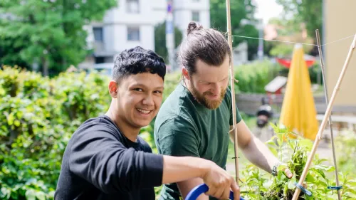 Minderjähriger Geflüchteter mit Pädagoge gießen das Kräuterbeet im Garten der Clearingstelle