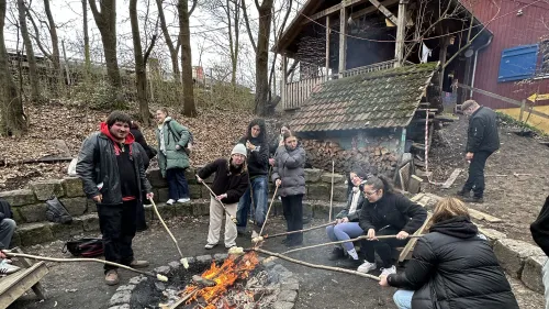 8 Schüler*innen mit Stockbrot am Lagerfeuer auf dem Aktivspielplatz Goldbachwiese